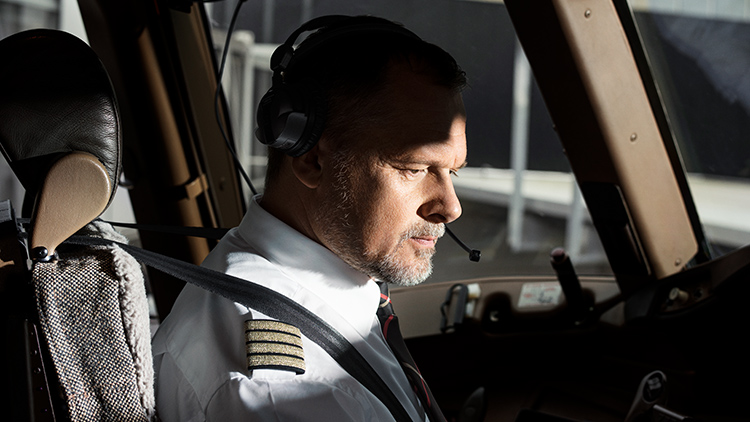 Ein älterer Pilot mit Vollbart schaut konzentriert auf  Instrumente in einem Flugzeugcockpit