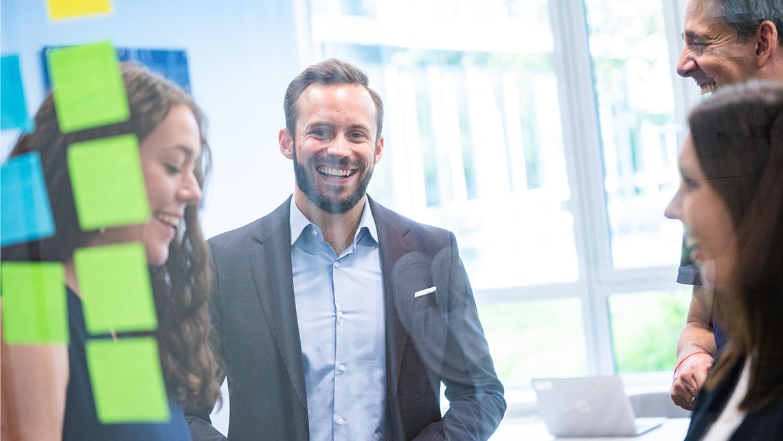 A group of laughing people stands behind a glass wall with coloured sticky notes on it