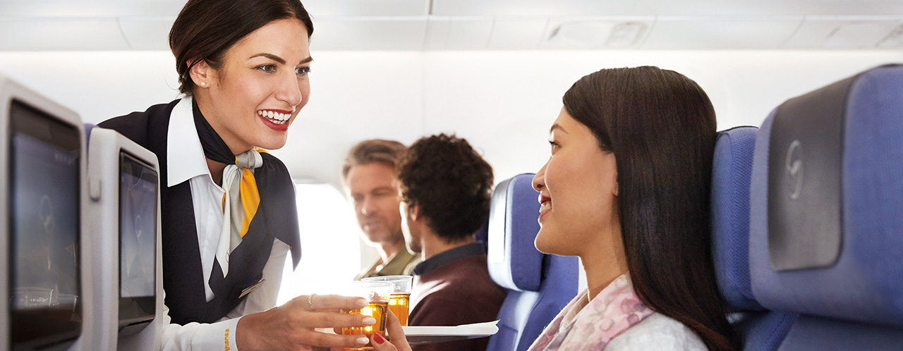 A flight attendant serves a passenger a drink during the flight