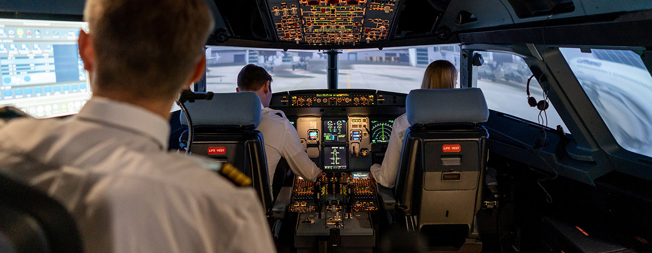 Blick in einen Cockpit-Simulator mit zwei Pilot:innen und einem Ausbilder