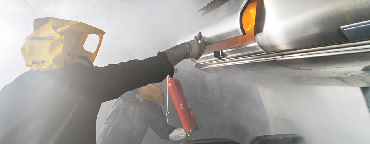 2 flight attendants wearing breathing masks train fire fighting in an aircraft cabin with fire extinguishers