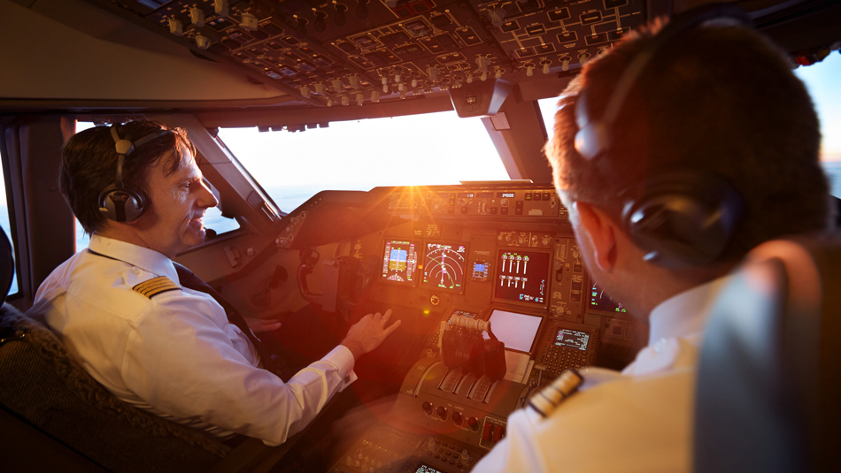 Two pilots sit in a cockpit during a flight while the sun shines in