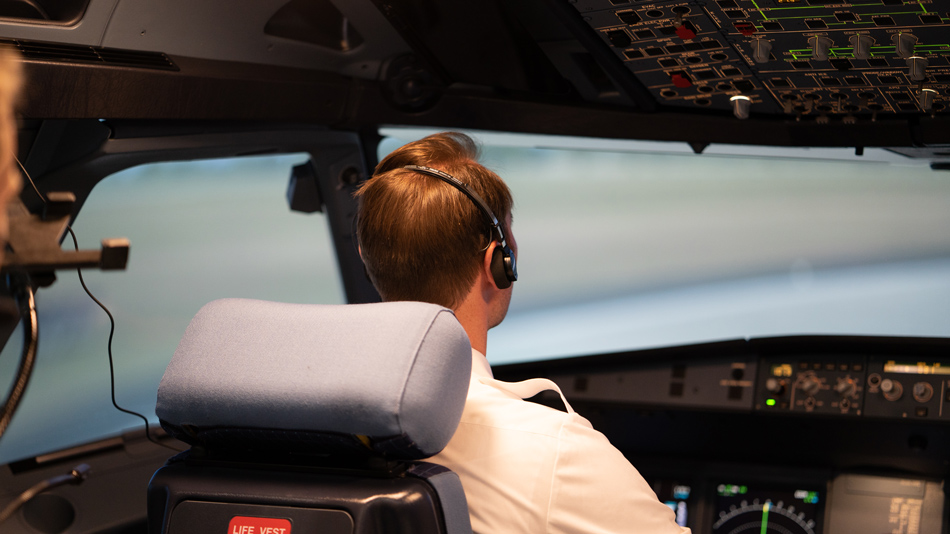 A pilot with headphones from behind in a cockpit simulator