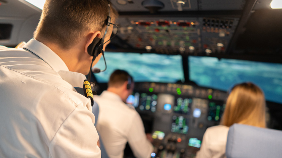 Ein Pilot als Trainer mit Kopfhörern beobachtet zwei Piloten während eines Trainings in einem Cockpit Simulator