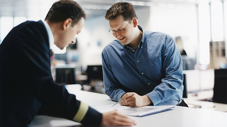 Zwei Männer, davon ein Pilot in Uniform, schauen gemeinsam auf Unterlagen