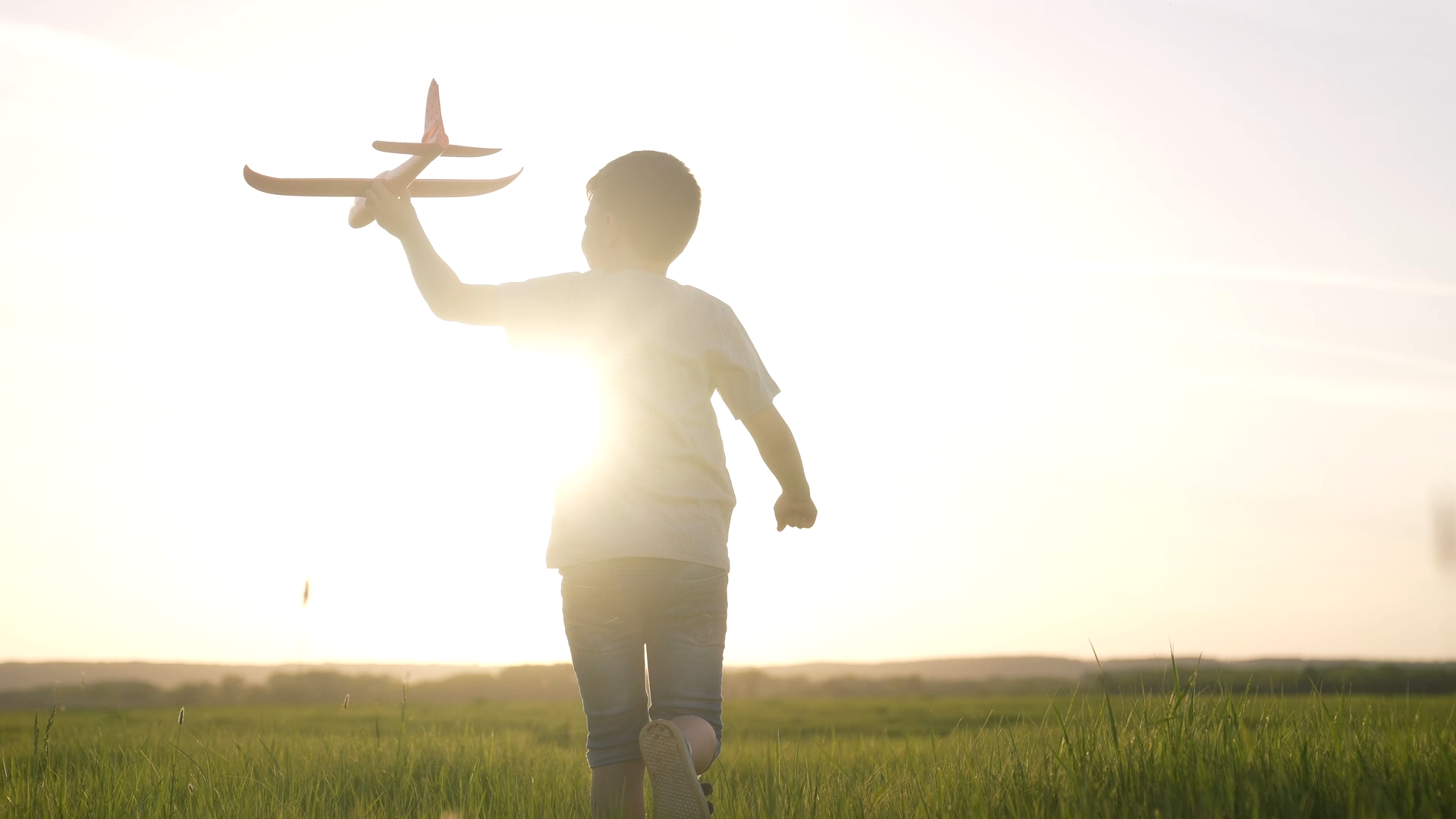 Ein Kind mit einem Modellflugzeug in der Hand läuft über eine Wiese.