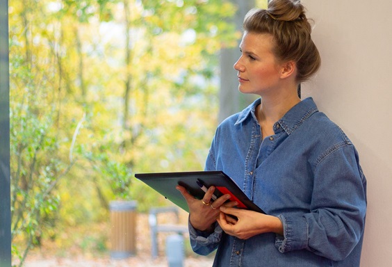 Eine Person steht an einem Fenster und hat ein Tablet in der Hand