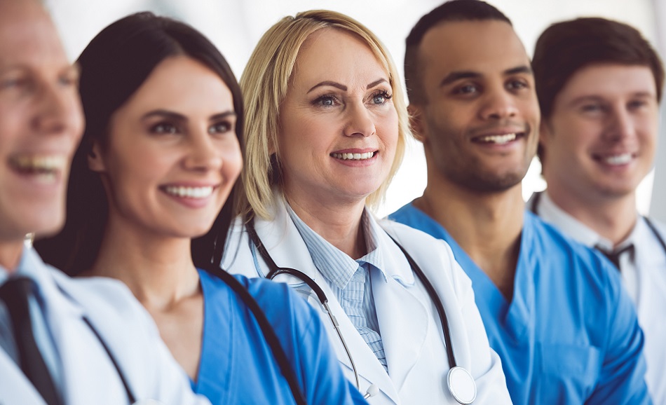 5 Ärzte und Pfleger in  blauen und weißen Kitteln stehen nebeneinander und lächeln.
