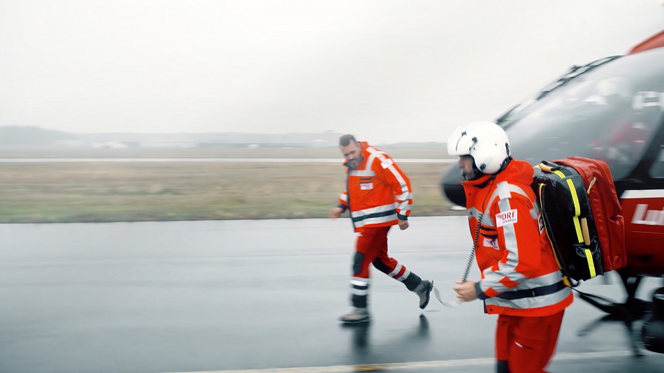 Zwei Sanitäter mit Notfallrucksack laufen von einem DRF Hubschrauber weg.