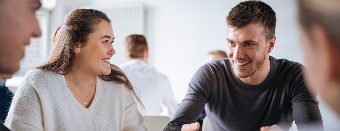 Three people are sitting at a table with a laptop in business clothes and have a conversation.