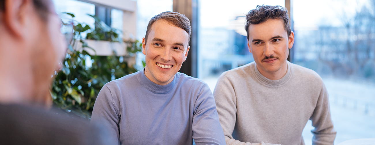  Three smiling people are standing around a table and looking at a laptop.