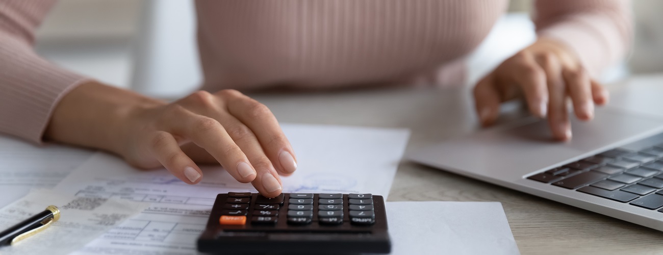 A person sits at a table and works at the same time on the calculator and laptop and finds out about the costs of pilot training.