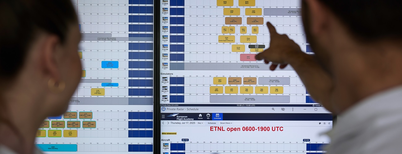 2 people sit in a flight simulator for a training aircraft. Outside there is a display showing a runway.