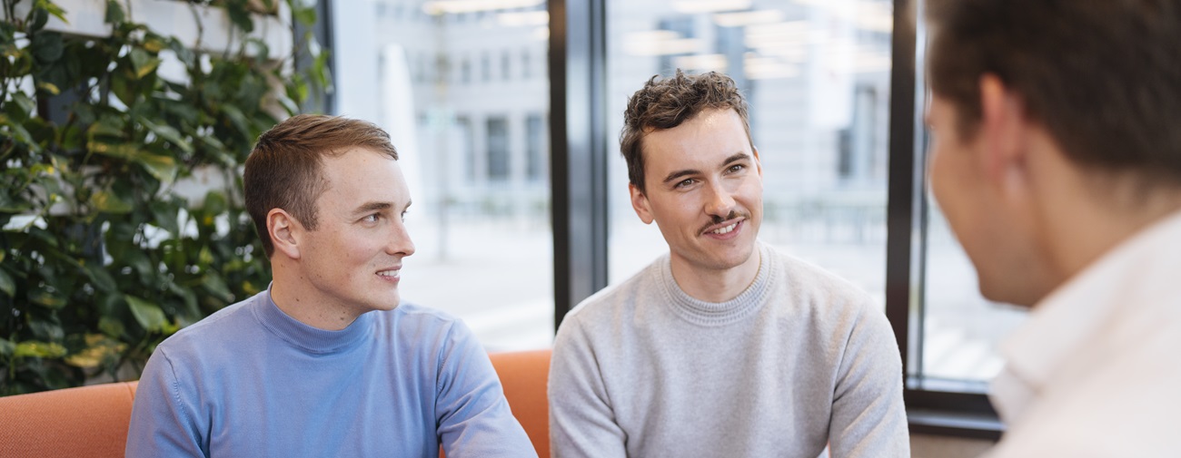 Fünf Personen in Business Kleidung sitzen an einem Tisch und halten ein Meeting ab.