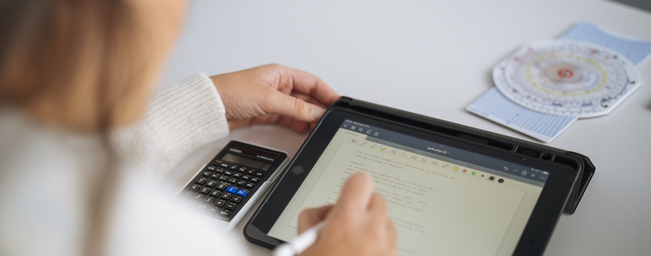 Eine Person sitzt an einem Tisch und arbeitet parallel am Taschenrechner und Laptop und informiert sich über die Kosten einer Pilotenausbildung.