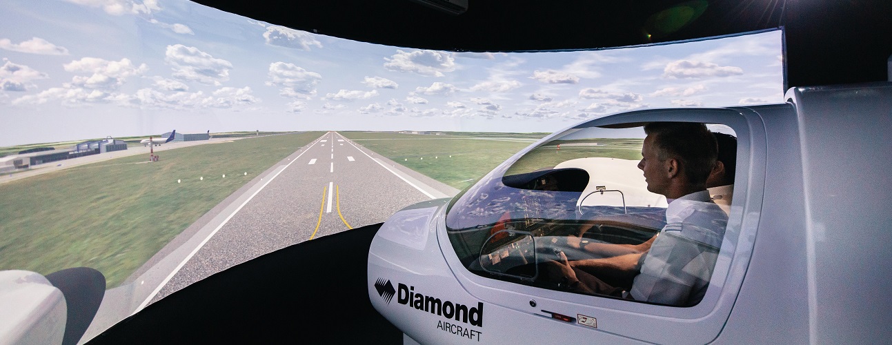 2 people sit in a flight simulator for a training aircraft. Outside there is a display showing a runway.