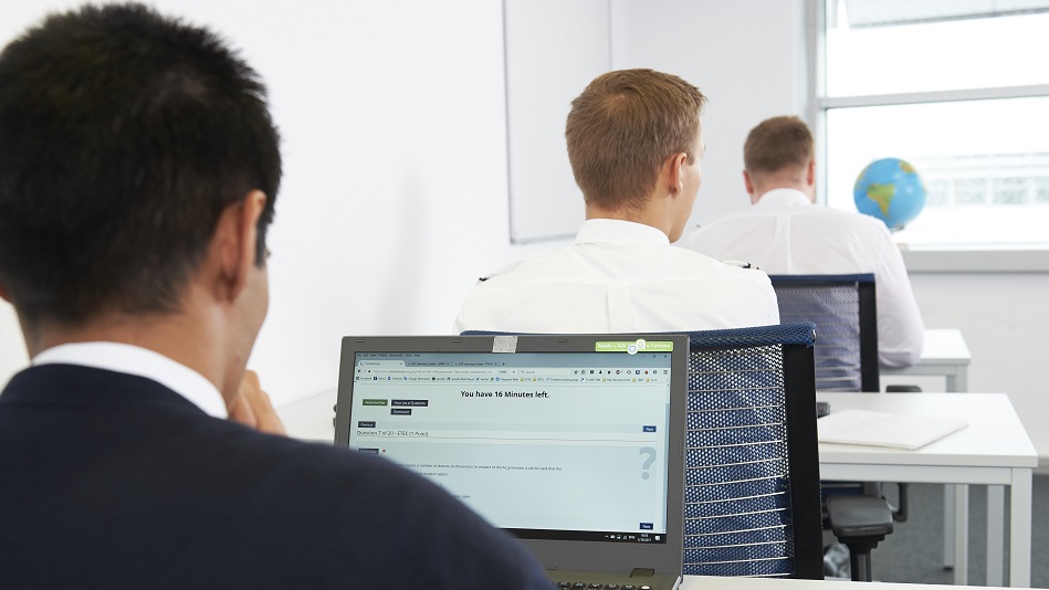 Three people sit one behind the other at tables in front of laptops and solve tasks