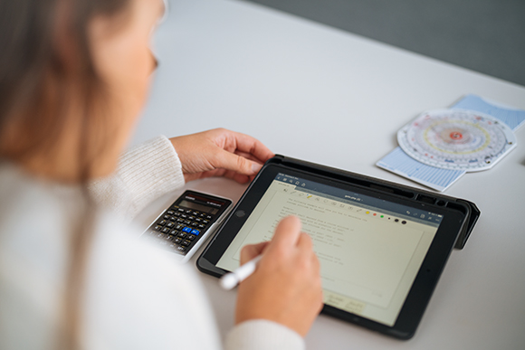 Eine Person sitzt an einem Laptop und hält in einer Hand einen Taschenrechner.