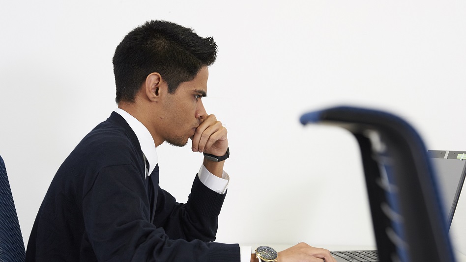 A person sits at a desk and writes an application on a laptop.