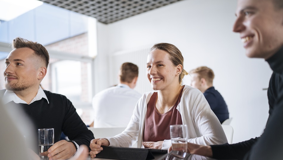 Mehrere Personen sitzen an einem Tisch und schreiben. Auf dem Tisch liegen Keyrings, Taschenrechner und Notizbücher.