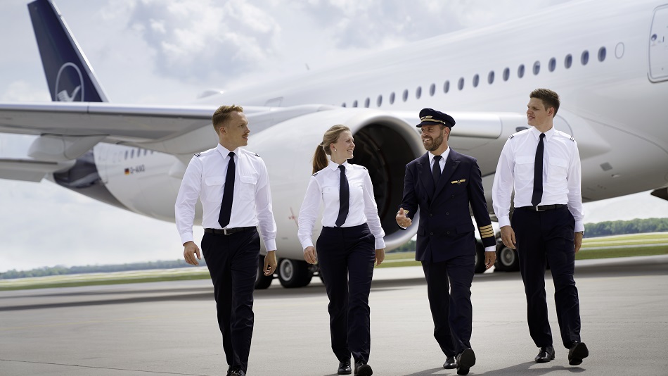 Eine Kapitän:in mit drei Flugschüler:innen laufen vor einem Airbus A350.