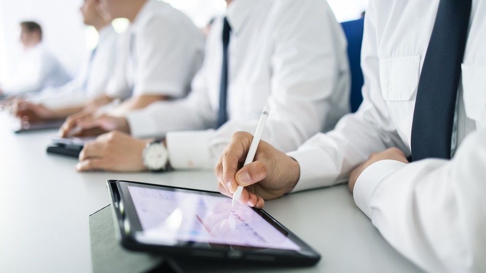  Several flight students are sitting at a table, in the foreground a flight student is working on a tablet.